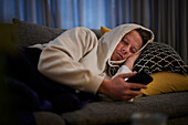 Kranker Mann auf dem Sofa liegend mit Smartphone