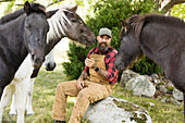 Männlicher Bauer zwischen Pferden sitzend