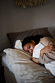 Pensive young woman lying in bed and hugging pillow