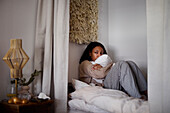 Pensive young woman sitting on bed and hugging pillow