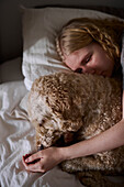 Weinende junge Frau, die einen Hund im Bett umarmt