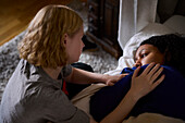 Young woman comforting friend lying in bed