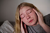 Junge Frau berührt Schläfe mit geschlossenen Augen
