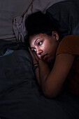 Nachdenkliche junge Frau im Bett liegend