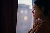 Pensive young woman looking through window