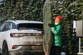 Lächelnde Frau mit Weihnachtsbaum in der Nähe des Autos