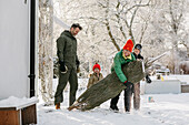Family carrying Christmas tree at winter