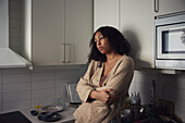 Pensive young woman standing in kitchen