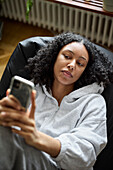 Young woman lying on bean bag and using phone