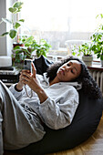 Young woman lying on bean bag and using phone