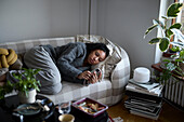 Pensive young woman lying on sofa and using phone