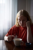 Pensive teenage girl sitting at table with cup of tea