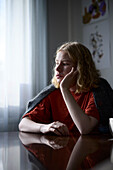 Pensive teenage girl sitting at table with hand on chin