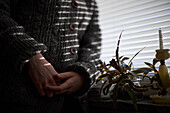 Close-up of teenage girl standing by window with clasped hands