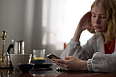 Pensive teenage girl sitting at table and using phone