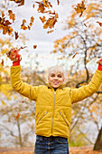 Smiling young woman throwing autumn leaves