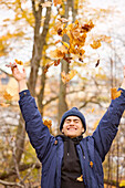 Smiling young man throwing autumn leaves