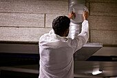 Rear view of man checking air duct