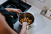 Woman's hands washing potatoes in saucepan