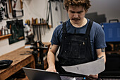 Blacksmith working with laptop and documents in his workshop
