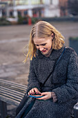 Young woman sitting on bench and using phone