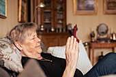 Ältere Frau auf dem Sofa mit Mobiltelefon