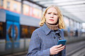 Frau mit Handy an der Straßenbahnhaltestelle