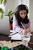 Girl doing homework with laptop at dining table