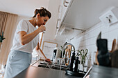Woman brushing teeth at kitchen sink