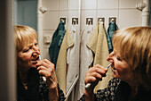Ältere Frau beim Zähneputzen vor dem Spiegel