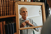 Senior man looking in mirror and buttoning shirt