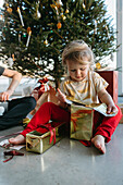 Mädchen öffnet Weihnachtsgeschenke unter dem Weihnachtsbaum