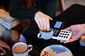 Young woman paying with phone in cafe
