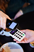 Young woman paying with phone in cafe