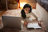 Mädchen macht Hausaufgaben mit Laptop auf dem Boden in ihrem Schlafzimmer