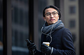 Handsome man with smartphone and paper cup on street