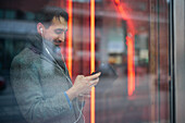 Eleganter Mann mit Smartphone, das sich im Fenster spiegelt