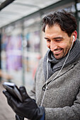 Eleganter Mann mit Smartphone an der Bushaltestelle