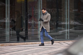 Elegant man with smartphone walking on street