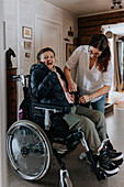 Mutter hilft Tochter im Rollstuhl beim Anziehen der Jacke