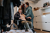 Mutter hilft Tochter im Rollstuhl beim Ausziehen des Mantels