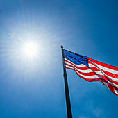 Low angle view of American flag waving in wind against clear sky with Sun