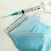 Syringe on Covid-19 vaccination record card and face mask