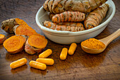 Turmeric powder, root and capsules on wooden surface