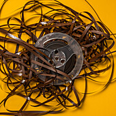 Overhead view of retro recording tape reel with unspooled tape against yellow background