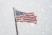 Zerrissene amerikanische Flagge am Fahnenmast mit fallendem Schnee