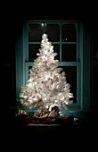 Beleuchteter weißer Weihnachtsbaum vor dem Fenster eines Hauses bei Nacht