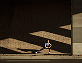 Woman stretching near brick wall in sunlight