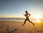 Frau joggt am Strand bei Sonnenuntergang