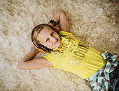 Porträt eines lächelnden Mädchens (10-11) mit Kopfhörern auf einem haarigen Teppich liegend